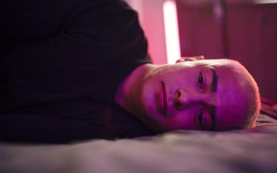 Depressed young man lying on bed in illuminated bedroom at home 