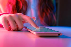 close up of teen girl with finger on iphone amidst pink and blue lighting