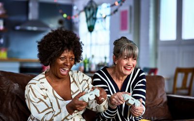 Two middle-aged women smile while holding video game controllers.