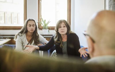  Mother sitting with daughter while sharing problems to male therapist at community center