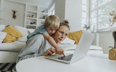 Boy doing mischief on laptop while standing behind mother at home