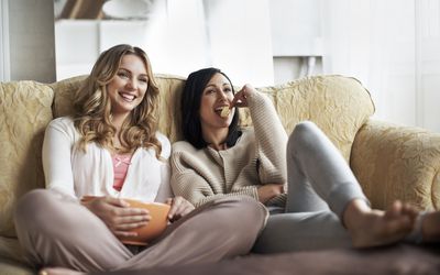 female friends watching movie on couch eating snacks