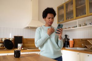 African American woman reading a text message in disbelief on mobile phone in the kitchen.
