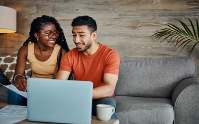 Young couple sitting in the living room at home and using a laptop to calculate their finances -