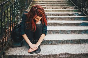 teenage girl with red hair sitting on stone steps looking sad