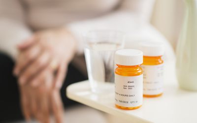 two pill bottles and glass of water with woman in background