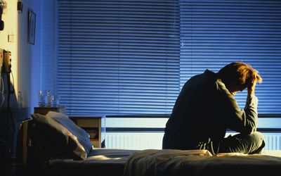 Distressed looking man sitting on hospital bed, head in hand, night