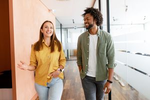 Couple of business people discussing tasks walking in the office hall. Two diverse colleagues have small talk during break. Friendly atmosphere in team