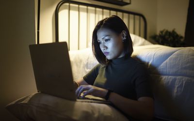 Woman working on her laptop in her bedroom at night