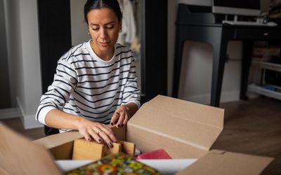 Young woman sitting on the floor at home organizing a moving box