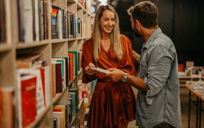 Side view of a smiling man and woman in the book store, looking for a good book to read.