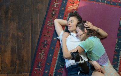 A lesbian couple lying on a rug on the floor and embracing each other affectionately.