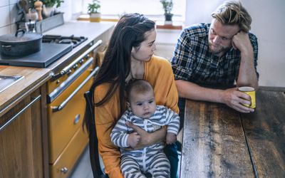 Serious looking family with baby sitting at kitchen table at home