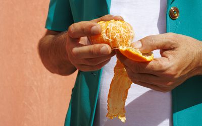 Man peeling orange fruit on sunny day