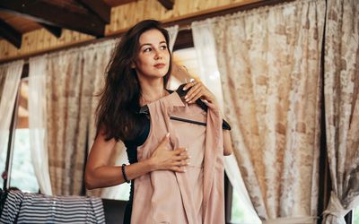 Young attractive woman organizing wardrobe and trying on clothes at home