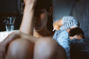 woman sits by the edge of the bed with her head in her hands