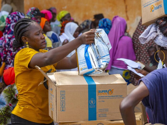 A distribution agent hands three packets of Corn Soya Blend (CSB) to a woman.