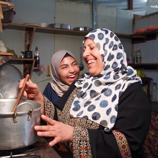 A refugee in Zaatari camp, alongside her teenage daughter, cooking a warm meal.