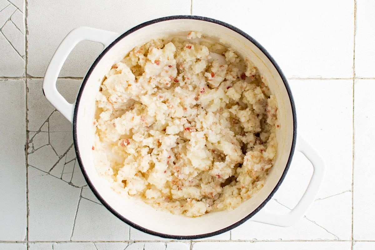 Mashed potatoes with bacon bits in a large white pot.