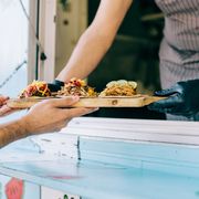 Man handing tray of tacos to another man from taco truck (Credit: Getty Images) thumbnail