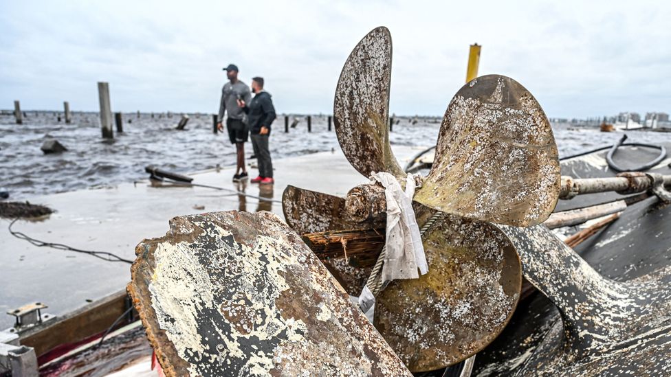 Broken rusted boat rudder by the shoreline, near two people (Credit: Getty Images)