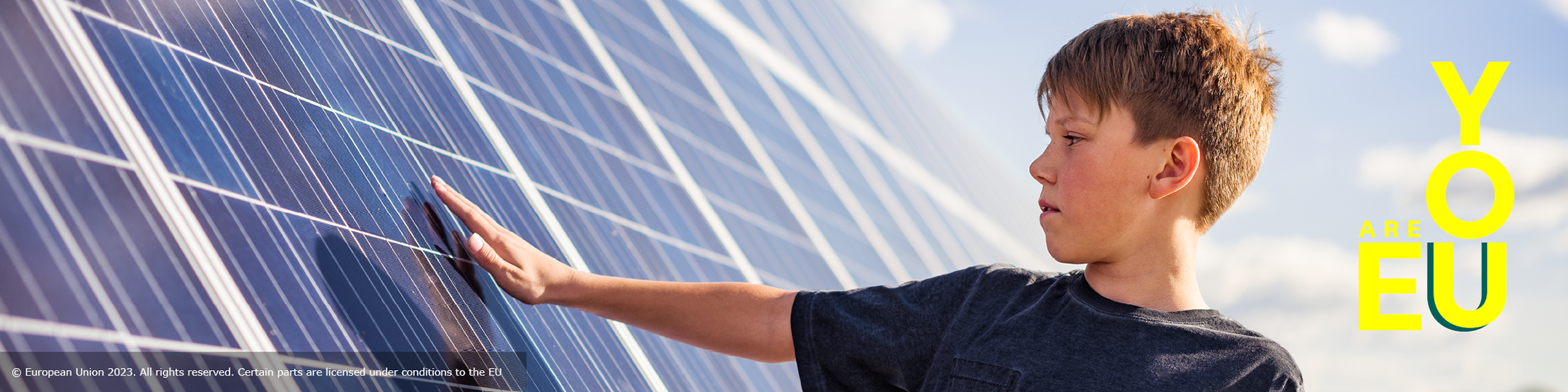 A young boy, viewed in side profile, extends his arm and hand towards a solar panel